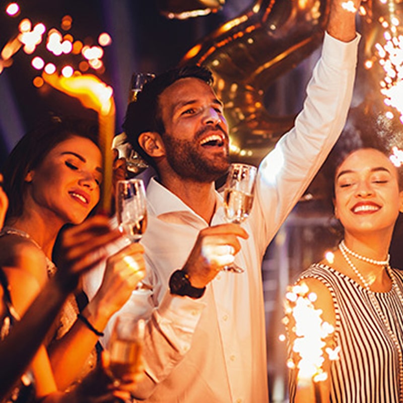 Célébration festive entre amis avec champagne et lumières Amis fêtant avec du champagne et des cierges magiques dans une ambiance joyeuse de soirée festive.