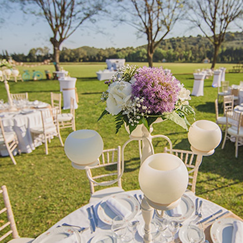 Mariage en Plein Air : Décoration de Table Élégante Décoration de table de mariage en plein air avec fleurs mauves et blanches sur une pelouse ensoleillée.