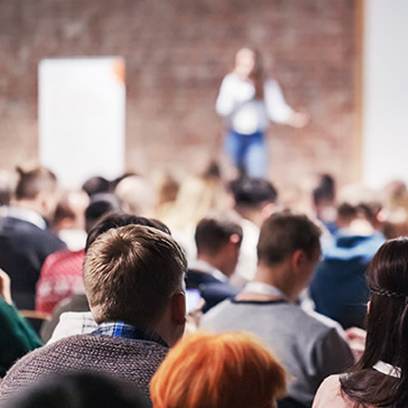 Conférence et Séminaire Professionnel : Public Attentif Audience écoutant une présentation lors d'un séminaire professionnel avec conférencier en arrière-plan.