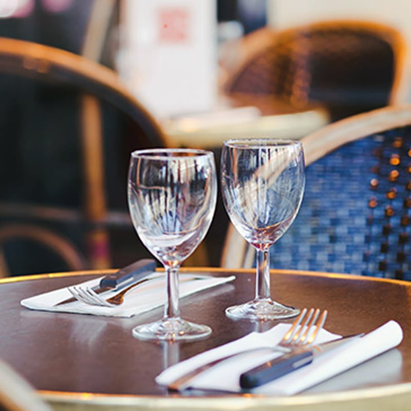 Table de bistrot avec verres à vin et couverts dressés Table de restaurant avec deux verres à vin et couverts sur serviettes blanches, ambiance bistrot parisien.